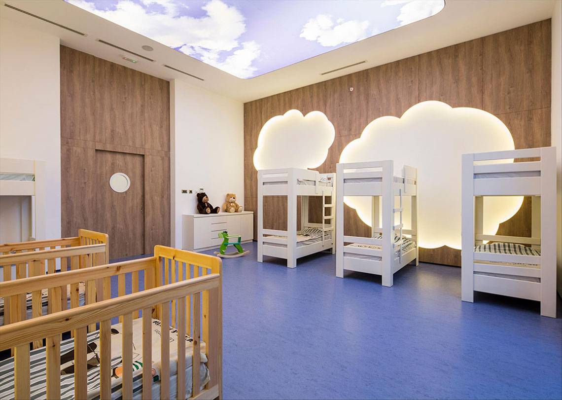 Kinderzimmer im Maxx Royal Kemer Resort mit mehreren Betten, Holzwänden und einer beleuchteten Wolkendecke.