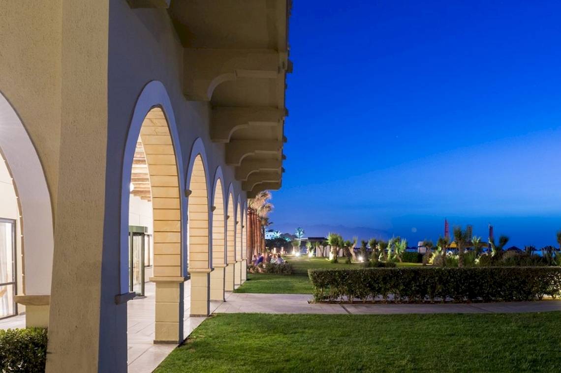 Außenansicht des Aquila Rithymna Beach Hotels bei Abend mit beleuchteter Gartenlandschaft.