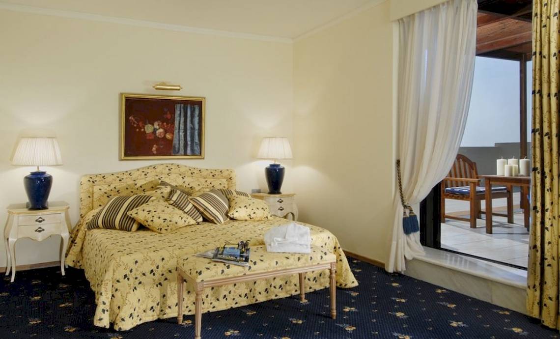 Schlafzimmer im Aquila Rithymna Beach Hotel mit gelber Bettwäsche, Nachttischen und Lampen.
