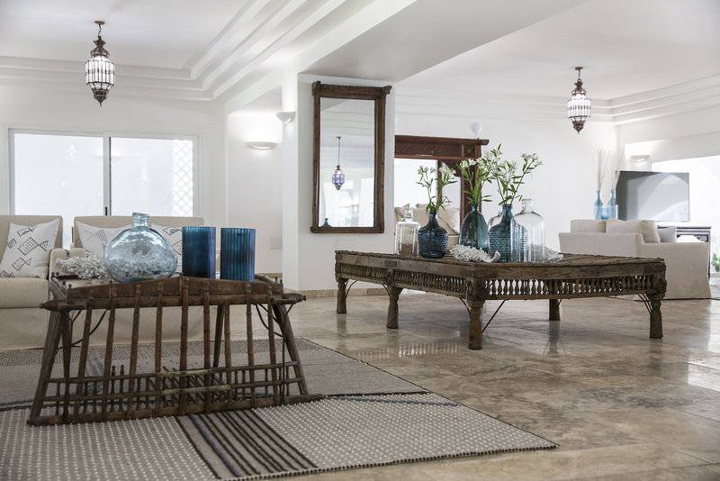 Wohnzimmer im Falkensteiner Resort Capo Boi mit zwei Sofas, Holztischen und blauen Vasen.