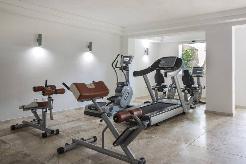 Fitnessraum im Falkensteiner Resort Capo Boi mit Geräten und Blick auf Außenbereich
