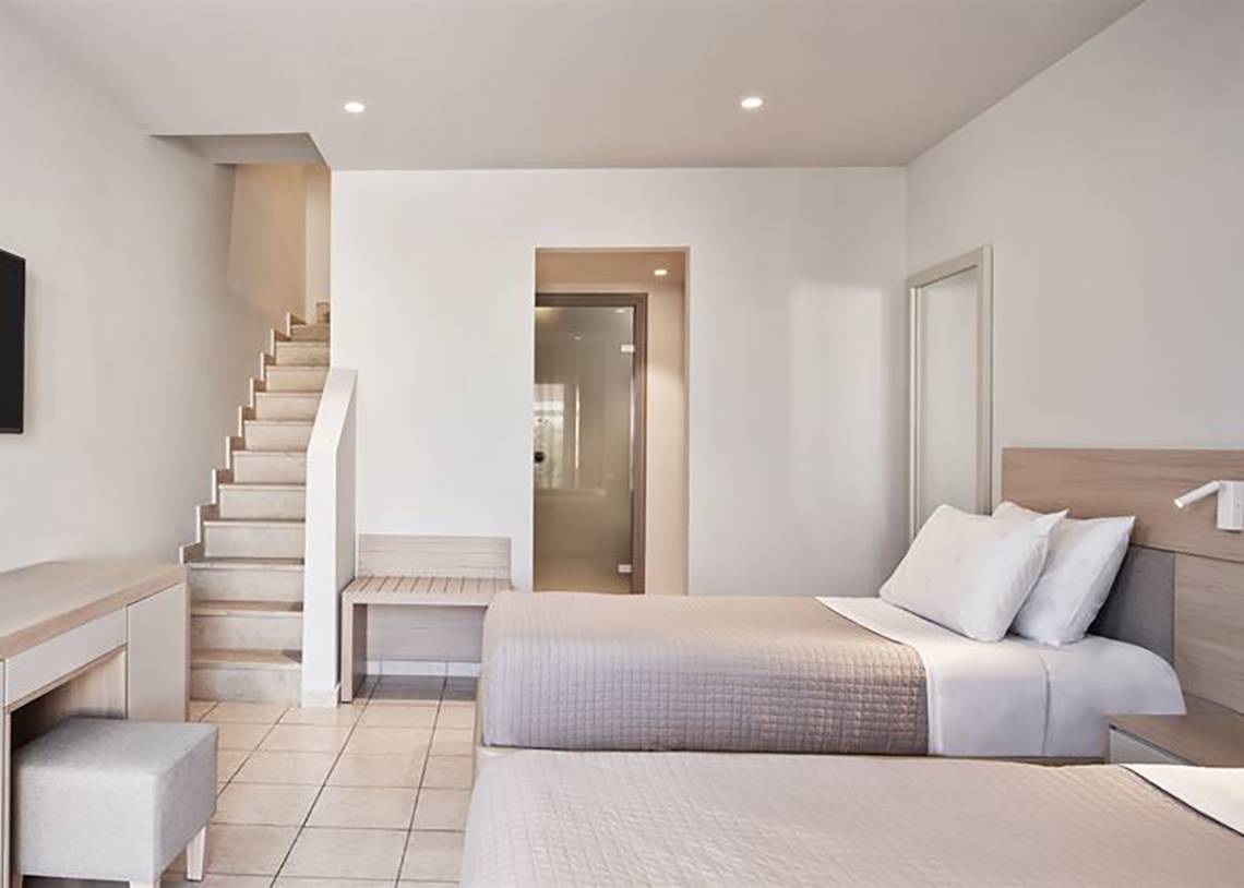Ein Schlafzimmer im Porto Bello Royal Hotel mit zwei Betten, einer Treppe und einem Fernseher.