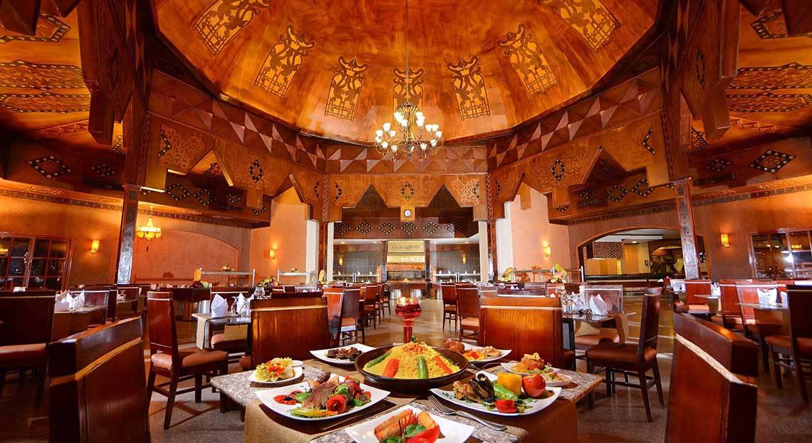 Innenansicht des Restaurants im Pickalbatros Jungle Aqua Park Resort mit runden Tischen, Holzstühlen und bunten Speisen.