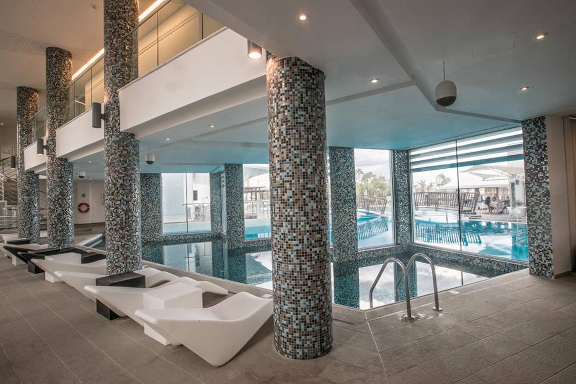 Pool-Loungebereich im Vassos Nissi Plage Hotel mit weißen Liegestühlen und gefliesten Säulen.