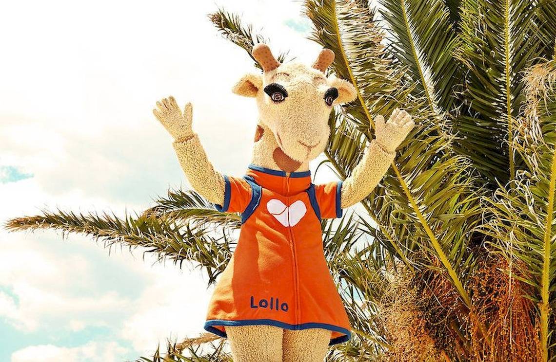 Maskottchen des Ostria Resort & Spa vor einer Palme, das ein orangefarbenes Outfit mit dem Wort Lollo trägt.