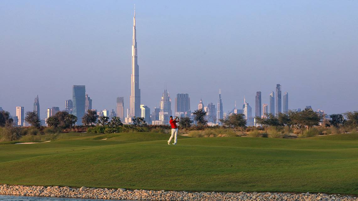 Golfplatz mit einem Spieler im Vordergrund und der Skyline von Dubai im Hintergrund.