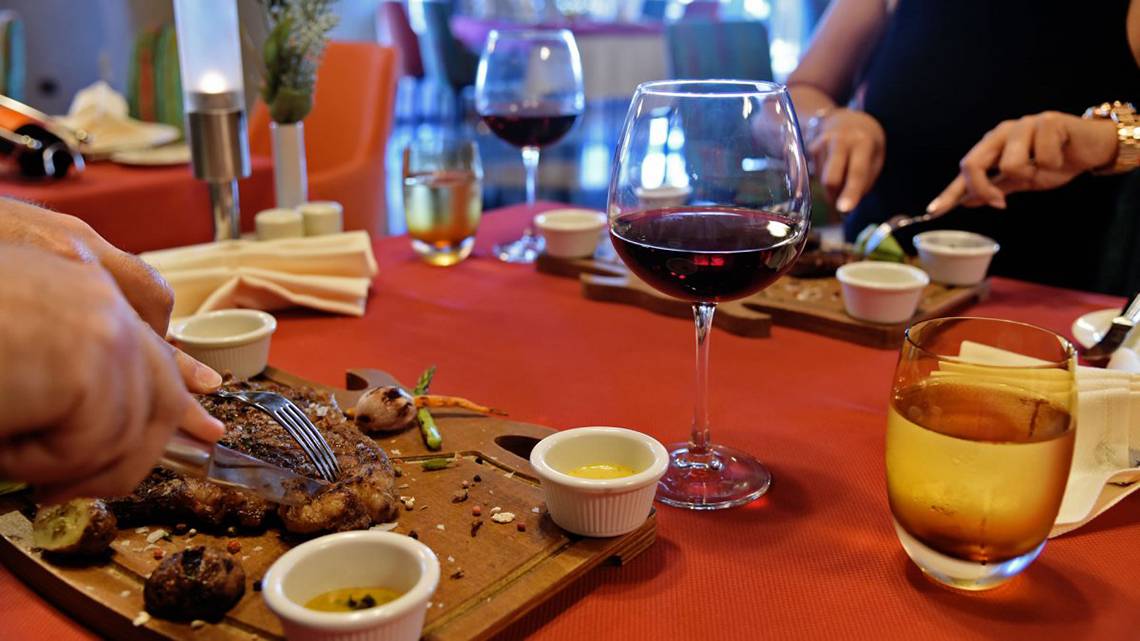 Personen essen am Tisch im Royal Wings Hotel mit Steak, Wein und Beilagen.