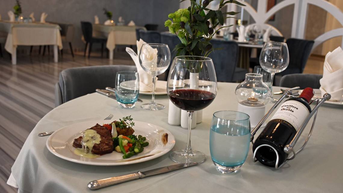 Ein Tisch im Royal Wings Hotel Restaurant mit einem Gericht, Weinglas und Wasserflasche.
