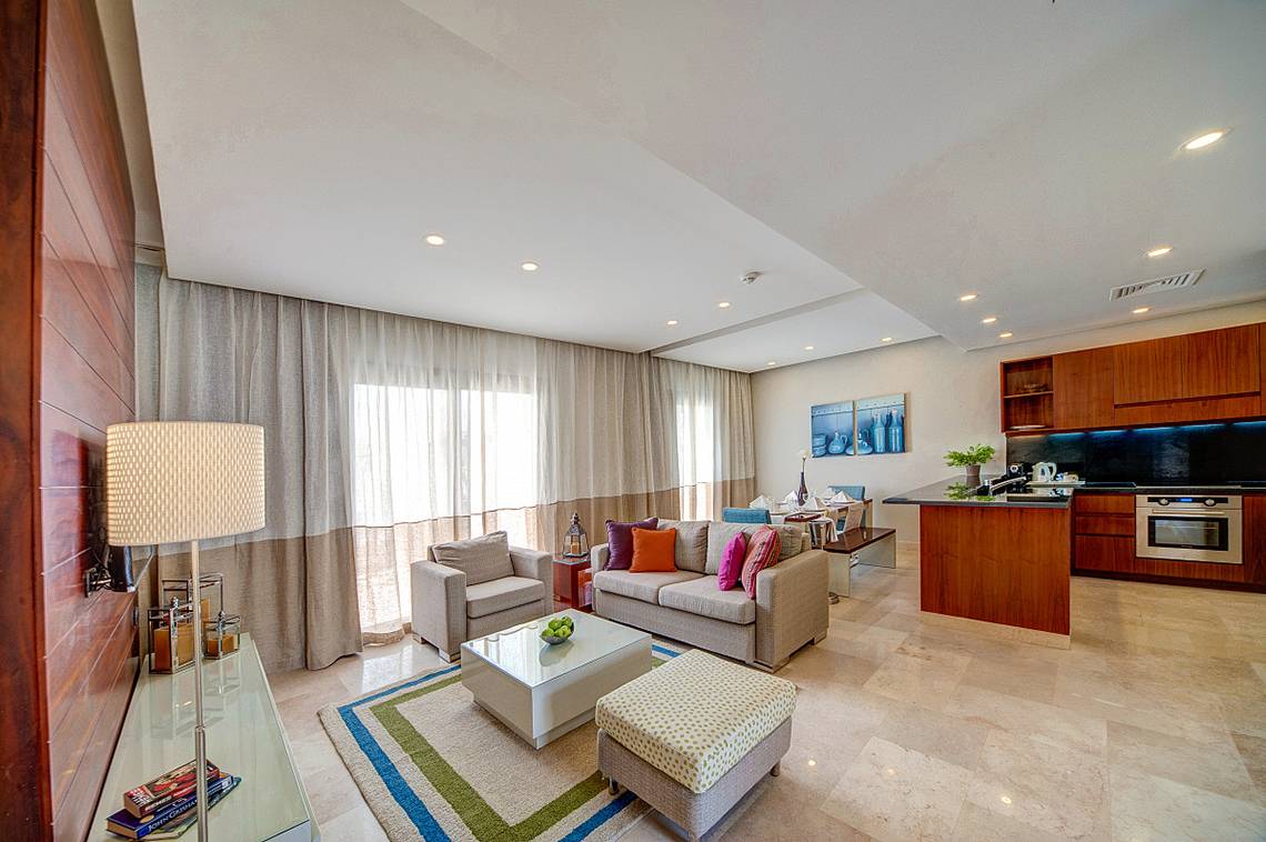 Wohnzimmer im Ancient Sands Golf Resort mit grauem Sofa, Couchtisch und blauem Teppich.