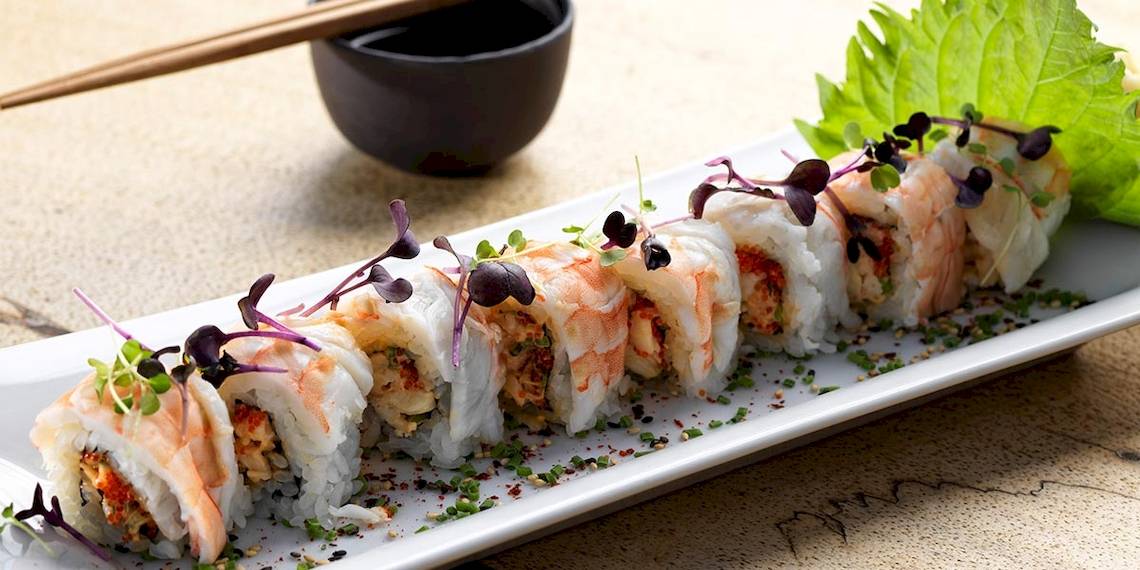 Ein Teller mit Sushi-Rollen, garniert mit kleinen Pflanzen, serviert mit Essstäbchen und einer Schüssel