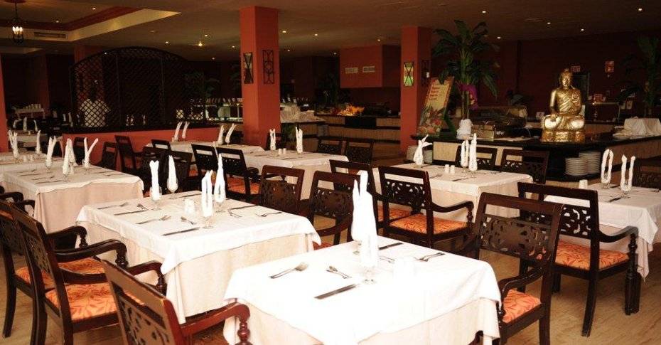 Innenansicht des Restaurants im Grand Palladium Jamaica Resort & Spa mit gedeckten Tischen, Stühlen und einem Buddha-Standbild.