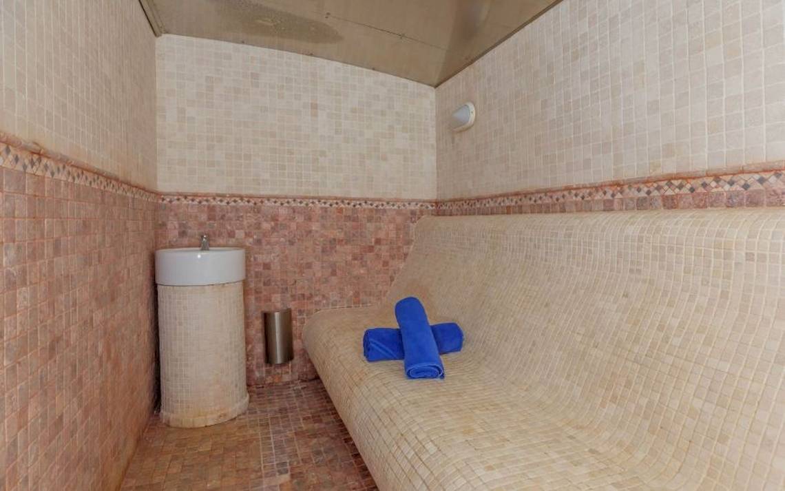 Saunabereich im Aparthotel Fontanellas Playa mit gefliesten Wänden, einer Bank, blauen Handtüchern und einem Waschbecken.
