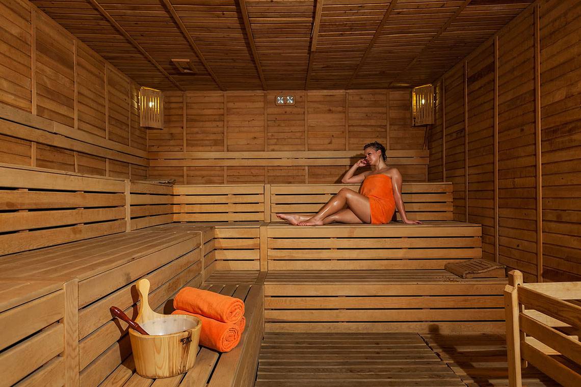 Eine Frau sitzt in einer Holzsauna des Sultan of Side Hotels und genießt die Wärme.