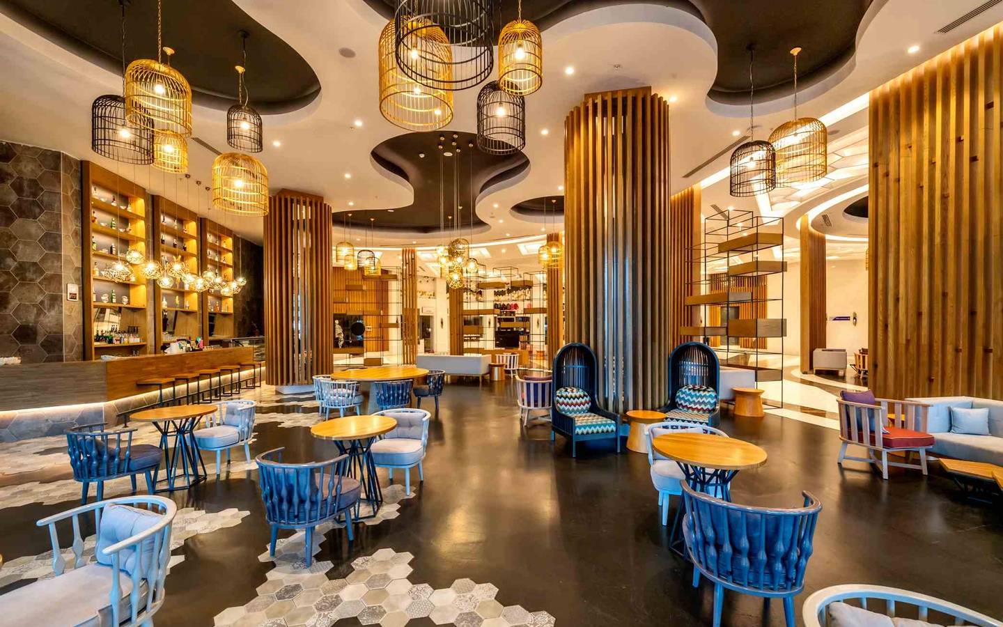 Loungebereich des Sidemarin Kirman Premium Hotels mit blauen Stühlen und Tischen, Holzsäulen und goldenen Pendelleuchten.