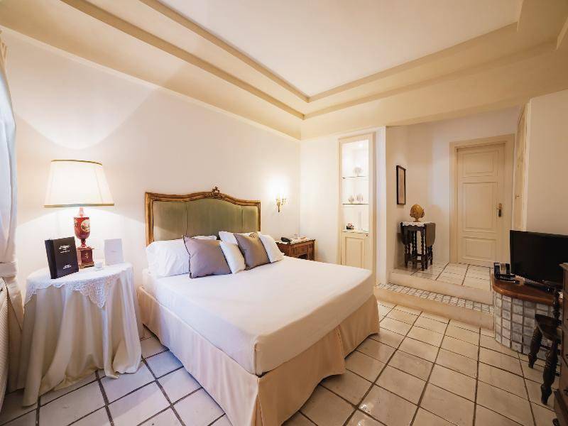Hotelzimmer von Il Melograno mit einem großen Bett, Kissen, Nachttisch mit Lampe und Fernseher.