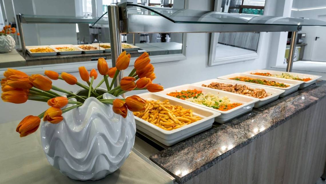 Buffettisch im Acharavi Beach Hotel mit verschiedenen Speisen und orangefarbenen Tulpen in einer weißen Vase.