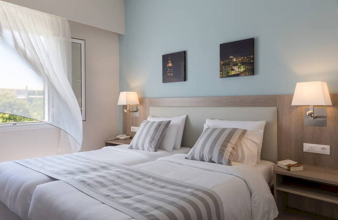 Doppelzimmer im Acharavi Beach Hotel mit zwei Betten, Nachttischen und Stadtbildern an der Wand.