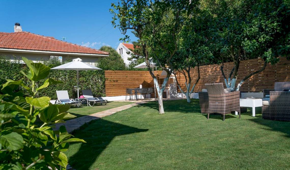 Außenbereich des Acharavi Beach Hotel mit Garten, Liegestühlen und Tischen