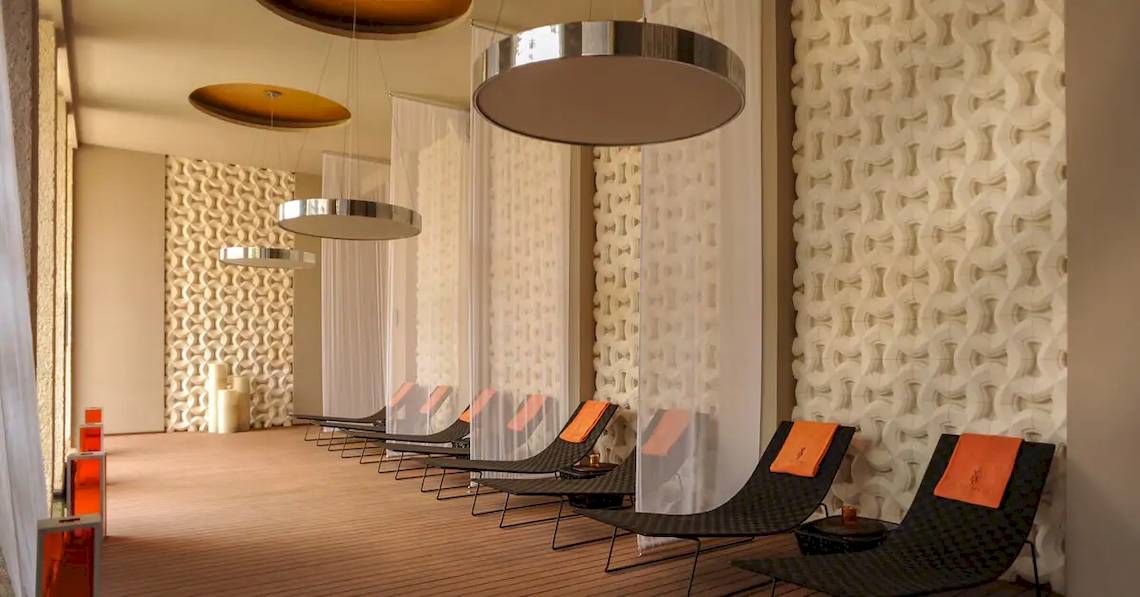 Spa-Lounge im Paradisus Playa del Carmen Hotel mit mehreren schwarzen Liegen und orangefarbenen Kissen.