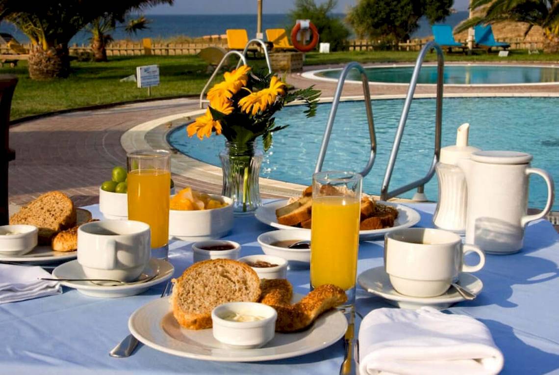 Frühstückstisch mit Orangensaft, Brot und Gebäck am Pool im Plaza Beach Hotel.