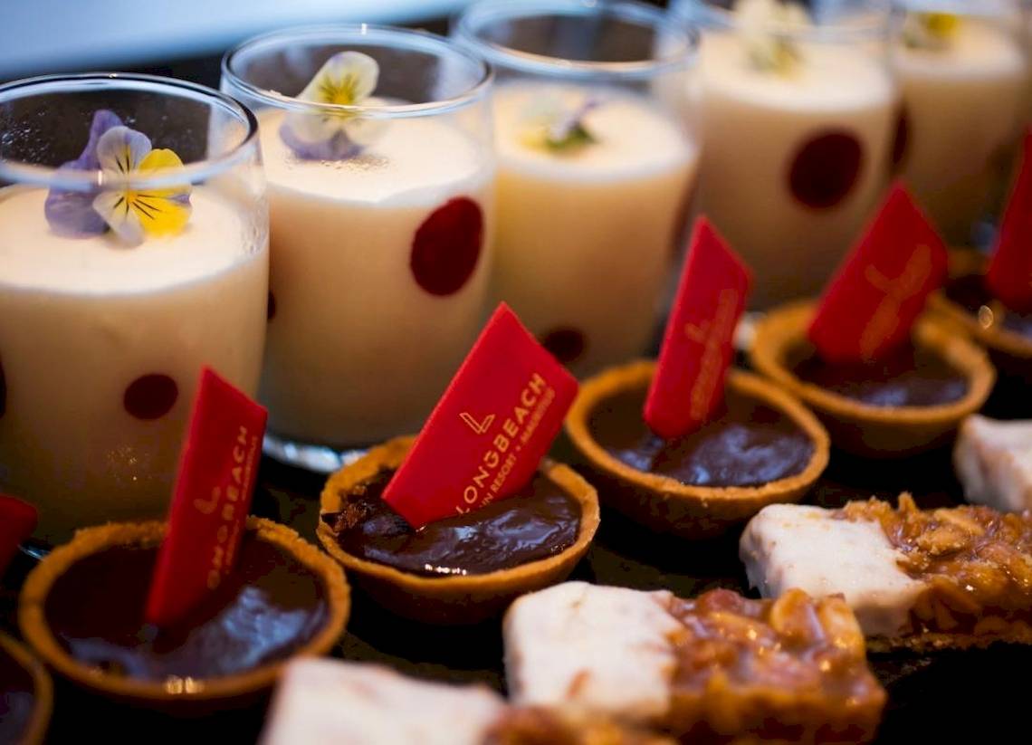 Desserts vom Long Beach Mauritius Resort, einschließlich Schokoladenkuchen und schaumiger Getränken mit Blüten.