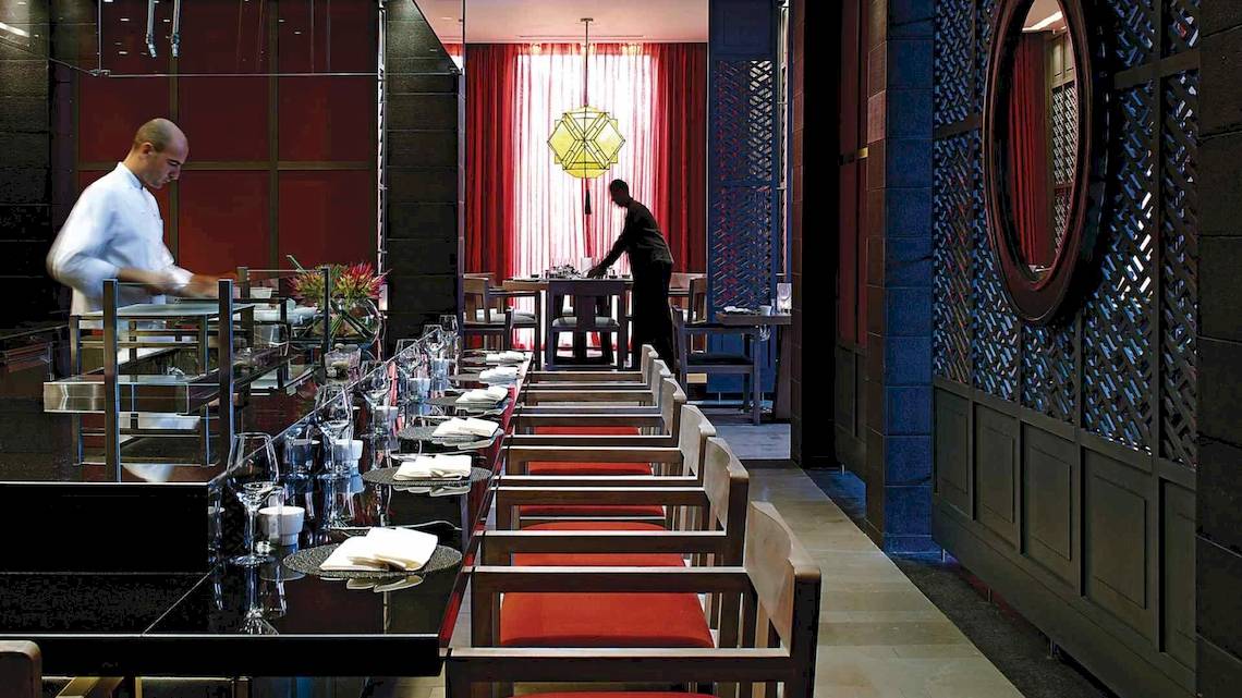 Ein Hotelrestaurant mit roten Stühlen und Tisch, an dem ein Kellner bedient.
