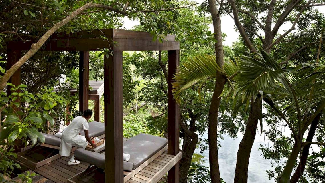 Eine Frau bereitet die Liegen auf der Holzterrasse im Wald des Long Beach Mauritius vor.
