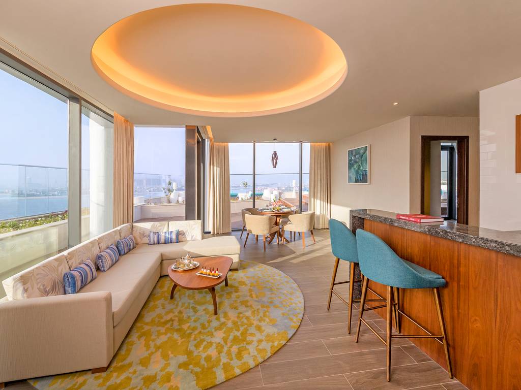 Wohnbereich im Retreat Palm Dubai MGallery by Sofitel mit modernem Design, großer Couch, Tisch und Blick auf die Stadt.
