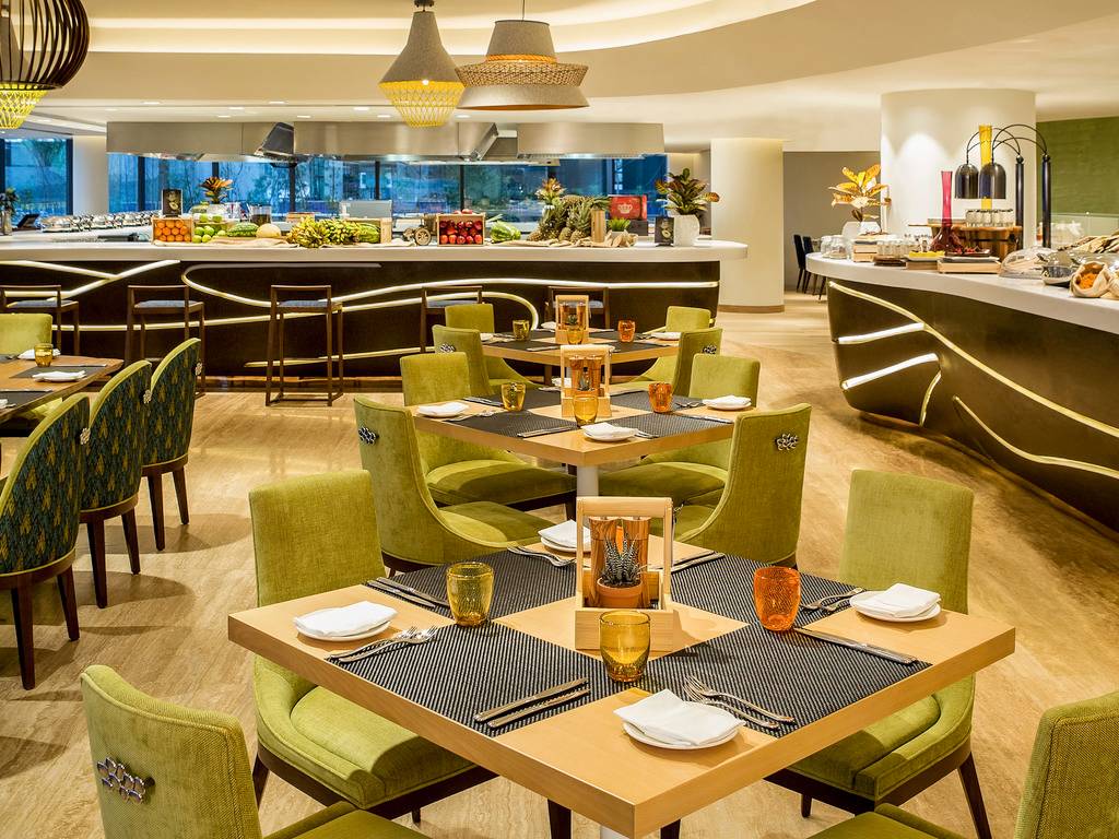 Speisesaal im The Retreat Palm Dubai MGallery by Sofitel mit grünen Stühlen und Tischen, Früchten und Dekorationen.