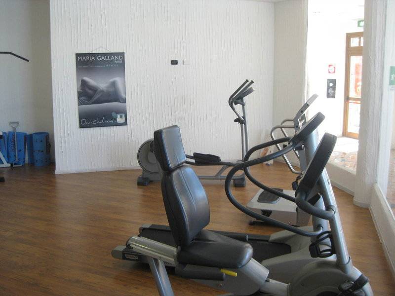Fitnessbereich im Baia Caddinas Hotel mit mehreren Cardiogeräten und einer Plakatwand.