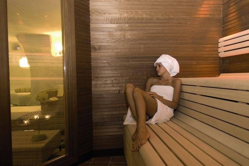 Eine Frau im weißen Handtuch sitzt auf einer Bank in der Sauna des Baia Caddinas Hotels.