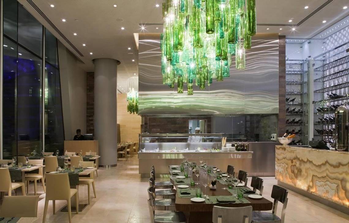 Innenansicht des Restaurants im W Abu Dhabi auf Yas Island mit grüner Kronleuchter und langen Esstischen.