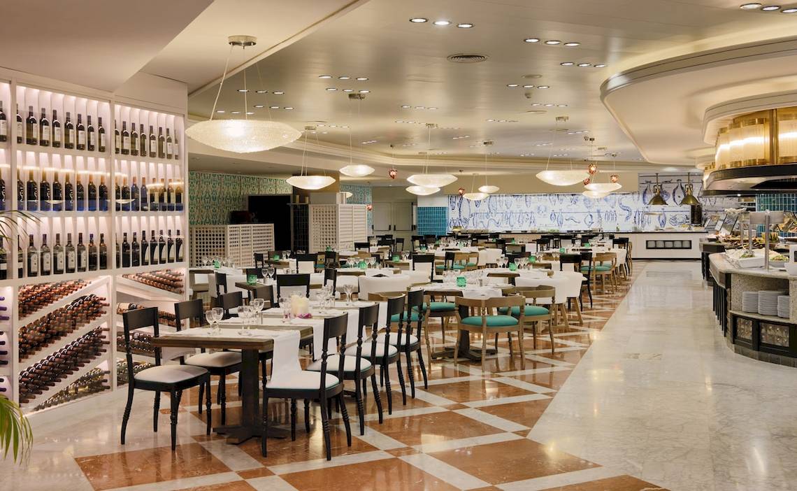 Innenansicht des Restaurants im H10 Timanfaya Palace Hotel mit gedeckten Tischen, Weinflaschen an der Wand und Kronleuchtern.