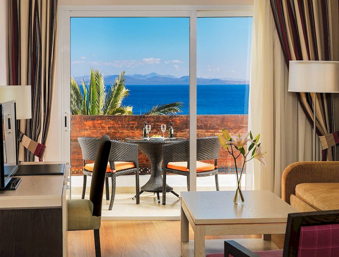 Aussicht von einem Zimmer im H10 Timanfaya Palace Hotel auf das Meer und eine Terrasse mit Tisch und Stühlen.