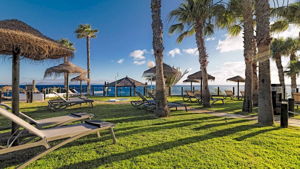 Das H10 Timanfaya Palace Hotel mit Liegestühlen und Sonnenschirmen am Strand.
