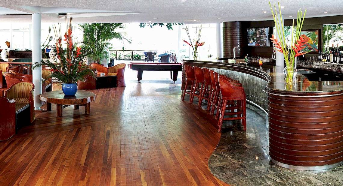 Innenansicht der Lobby-Bar des Barcelo Tambor Hotels mit Holzboden, roten Stühlen, Tisch mit Pflanze und Billardtisch.