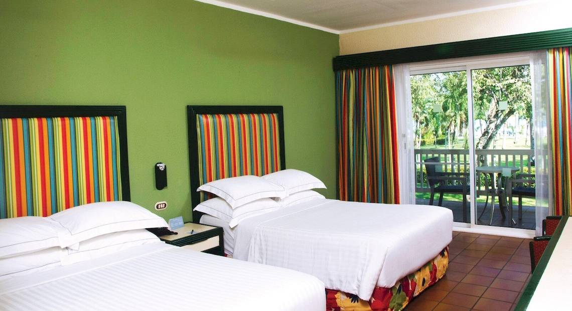 Zwei Betten im Hotelzimmer des Barcelo Tambor mit grünen Wänden und bunten Kopfteilen.