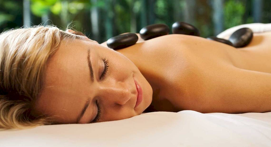 Eine Frau genießt eine Massage im Spa, mit Steinen auf dem Rücken liegend.