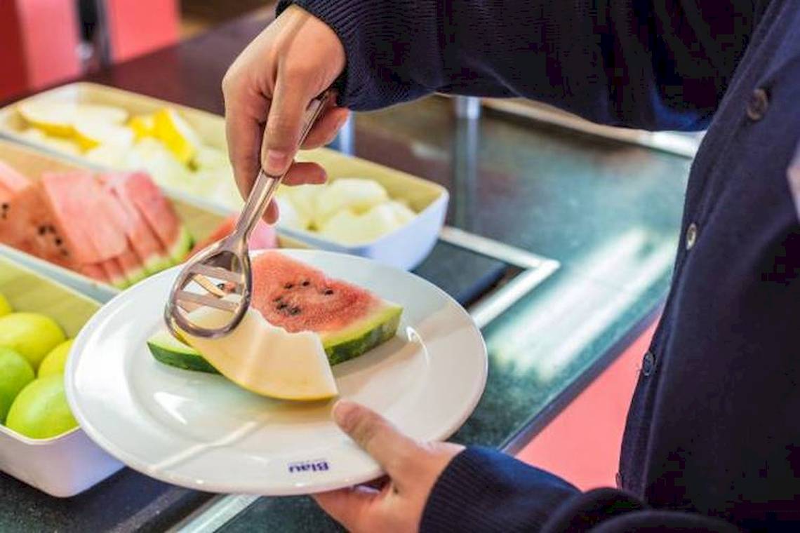 Eine Hand schneidet eine Wassermelone auf einem Teller im Buffet.