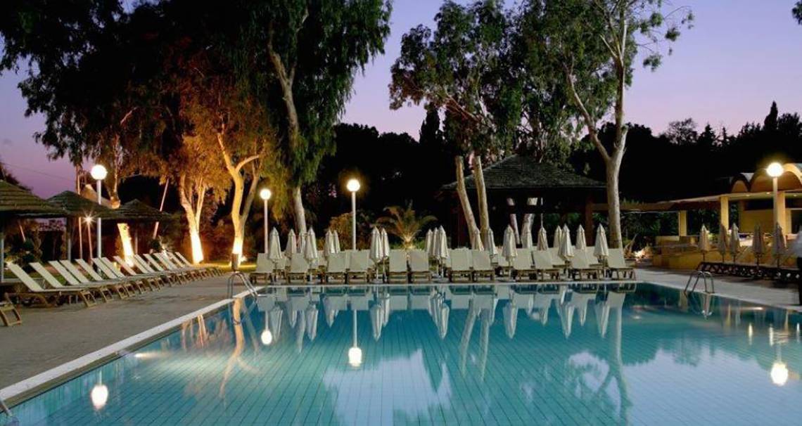 Abendansicht des Schwimmbeckens im Atlantica Miramare Beach Hotel mit illuminierten Liegen und Schirmen