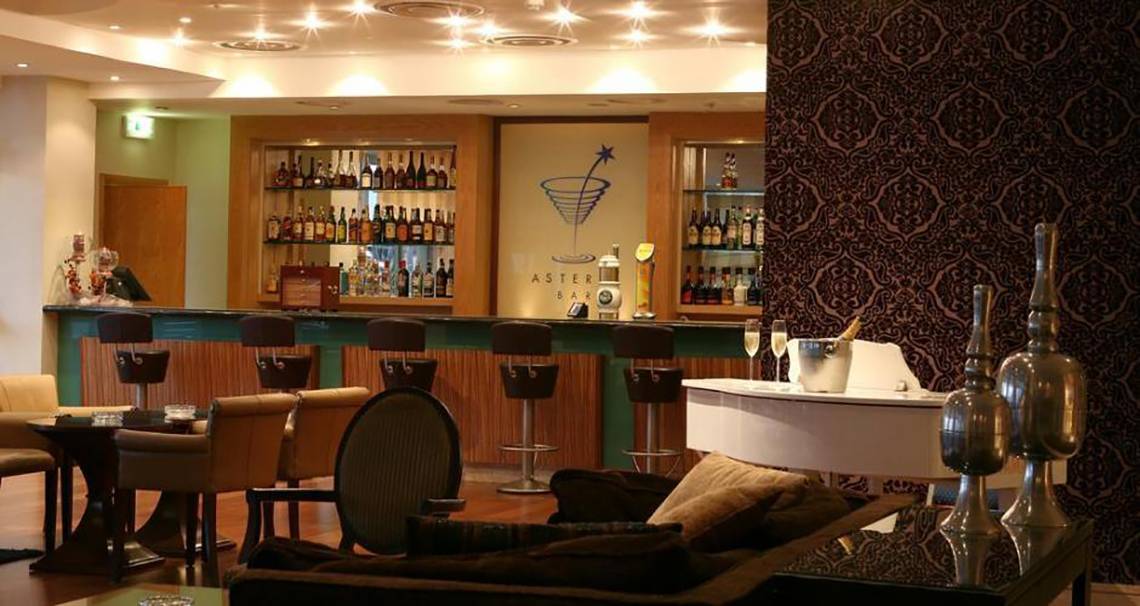 Innenansicht der Bar im Atlantica Miramare Beach Hotel mit Theke, Stühlen und Flaschen.