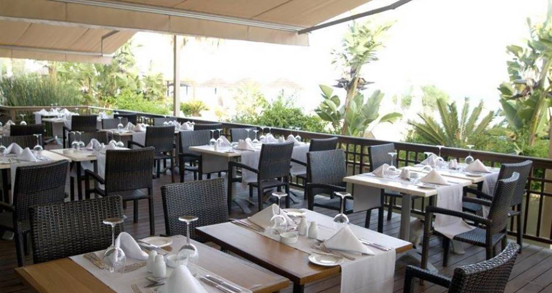 Terrasse des Atlantica Miramare Beach Hotels mit eingerichteten Tischen und Stühlen im Freien.