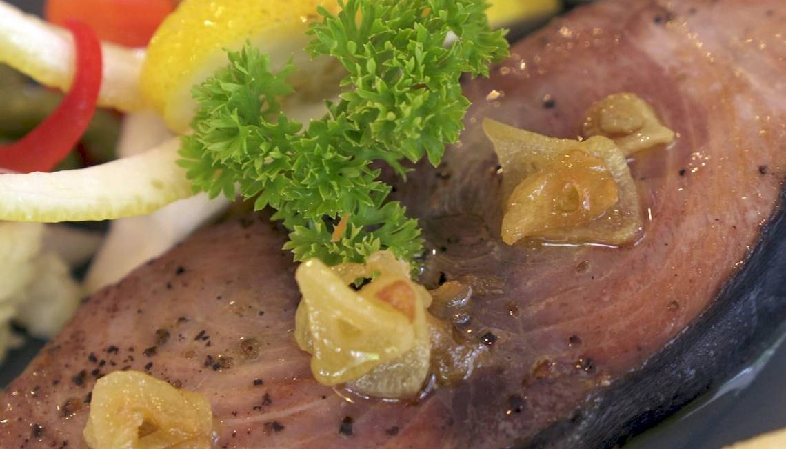 Nahaufnahme von gegrilltem Fisch mit getrockneten Tomaten und frischer Petersilie, serviert im Nika Island Resort & Spa.