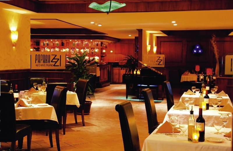 Innenbereich des Paparazzi Restaurants mit Tisch, Stühlen, Weinflaschen und Dekoration.