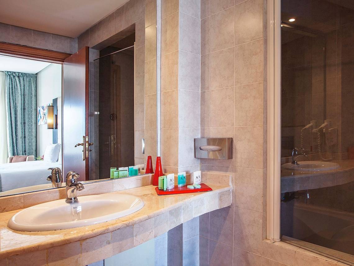 Badezimmer im Bianca Beach Resort mit Spiegel, Waschbecken und Duschbereich.