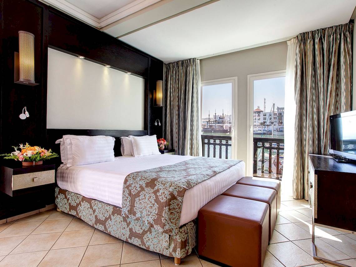 Innenansicht eines Hotelzimmers im Bianca Beach Resort mit Bett, Nachttischen, Fernseher und Balkon.