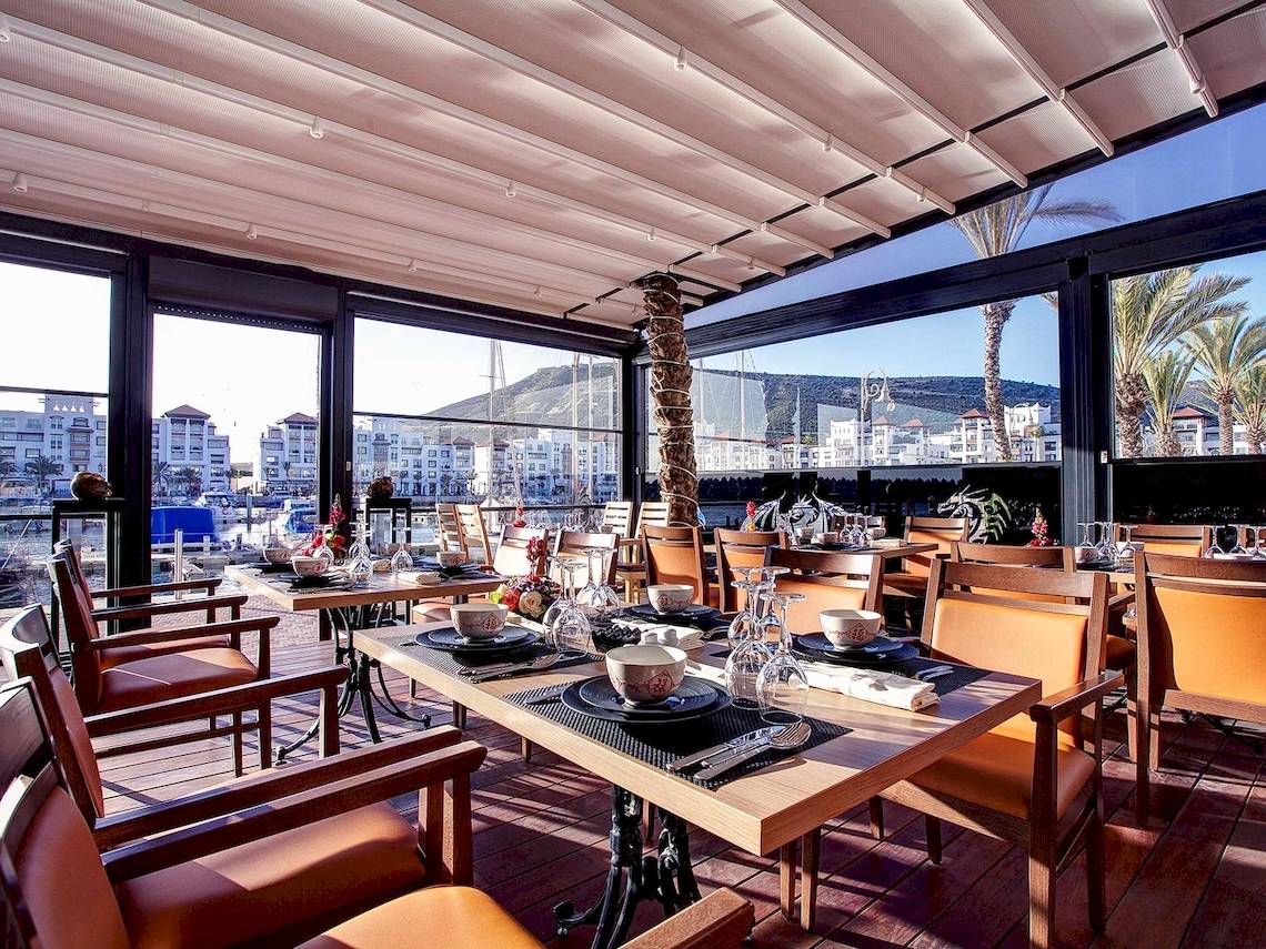 Innenansicht des Restaurants im Bianca Beach Resort mit Tischen und Stühlen, Aussicht auf die Stadt und Berge.