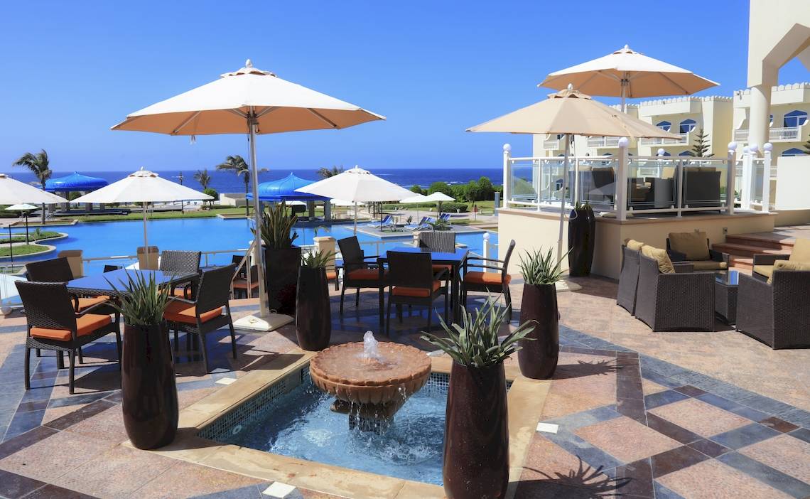 Pool-Terrasse im Wyndham Garden Salalah Mirbat mit Tischen, Stühlen und Sonnenschirmen