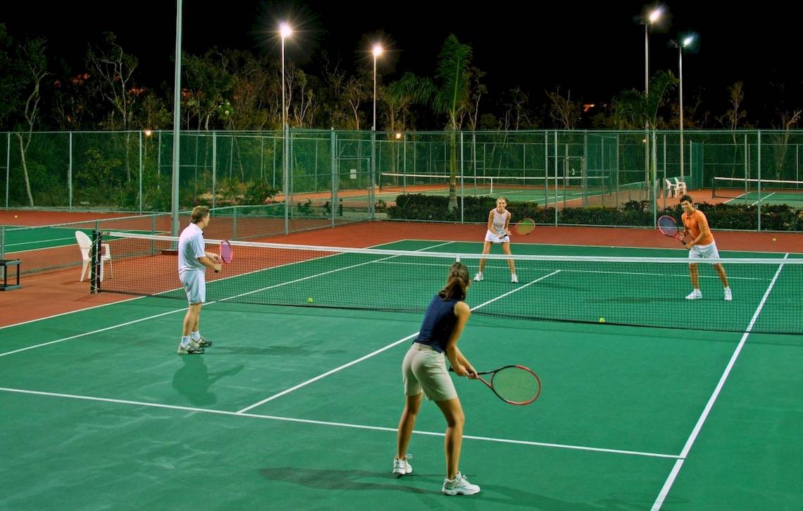 Spieler spielen Tennis auf einem beleuchteten Tennisplatz bei Nacht.