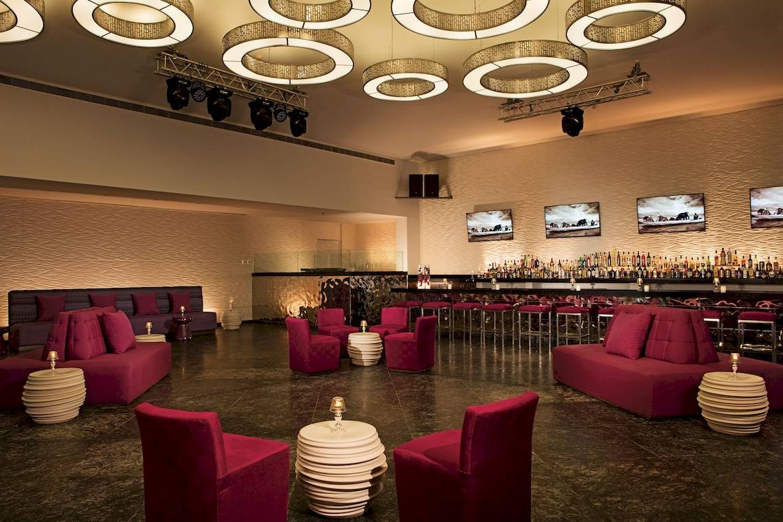 Loungebereich im Hotel Secrets Akumal Riviera Maya mit roten Stühlen, Sofas und einer Bar.